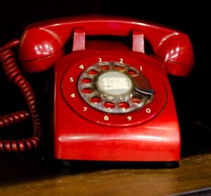 A classic red rotary telephone exuding nostalgia, set on a wooden shelf indoors.
